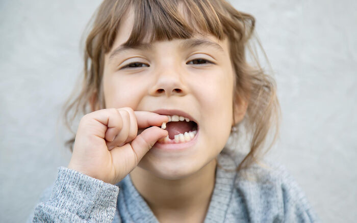 Young child holding a lost tooth and smiling, illustrating random things people did as kids that seem unusual now.