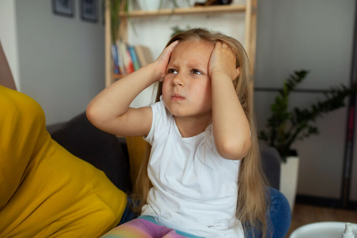 Young girl sitting indoors holding her head, reflecting on random things people did as kids that weren’t normal.
