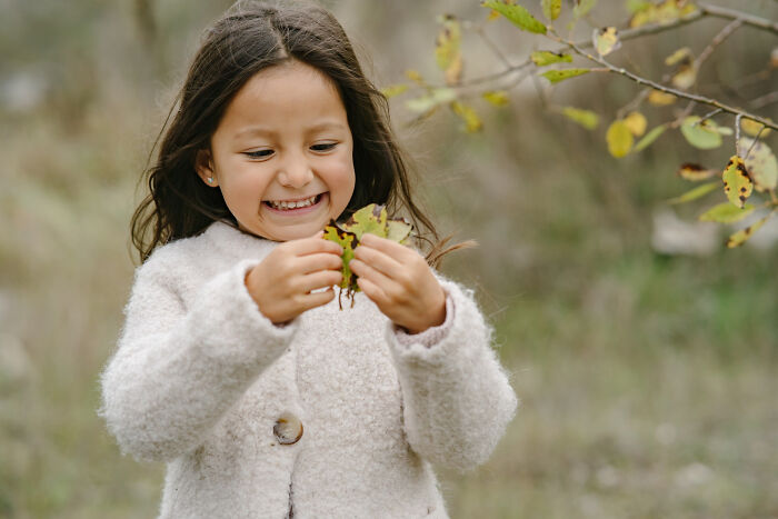 Young girl smiling outdoors, holding leaves, capturing random things people did as kids that weren’t exactly normal