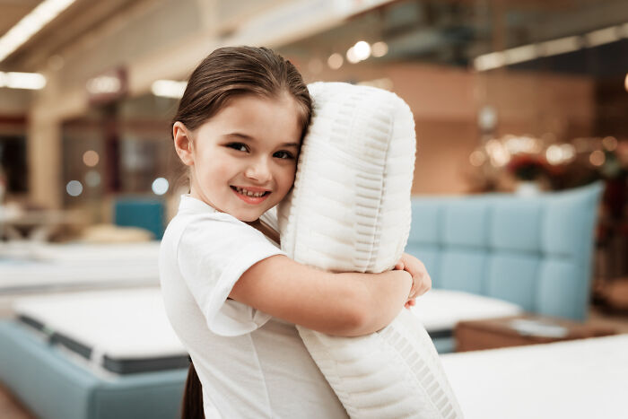 Young girl smiling and hugging a pillow, illustrating random things people did as kids that weren’t exactly normal.