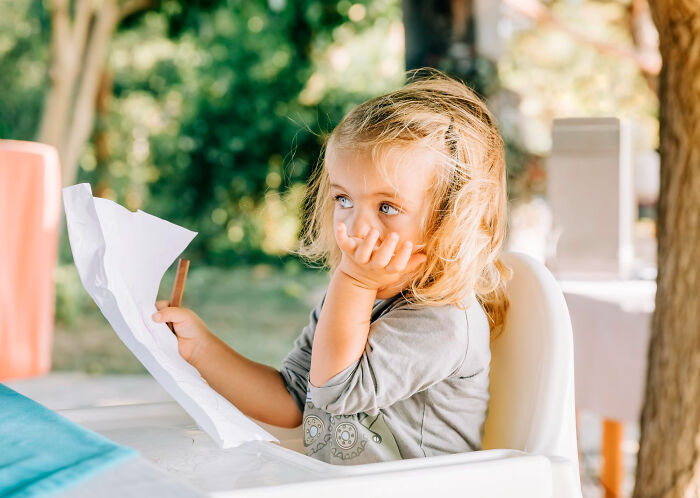 Young child sitting outdoors holding a crumpled paper, reflecting on random things kids did that weren't normal.
