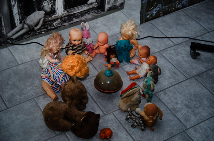 A circle of assorted vintage dolls and stuffed toys on a tiled floor, evoking random childhood things.