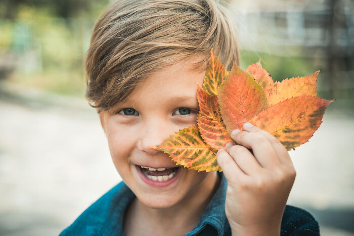 Smiling child holding colorful autumn leaves up to face, illustrating random things people did as kids that weren’t normal.