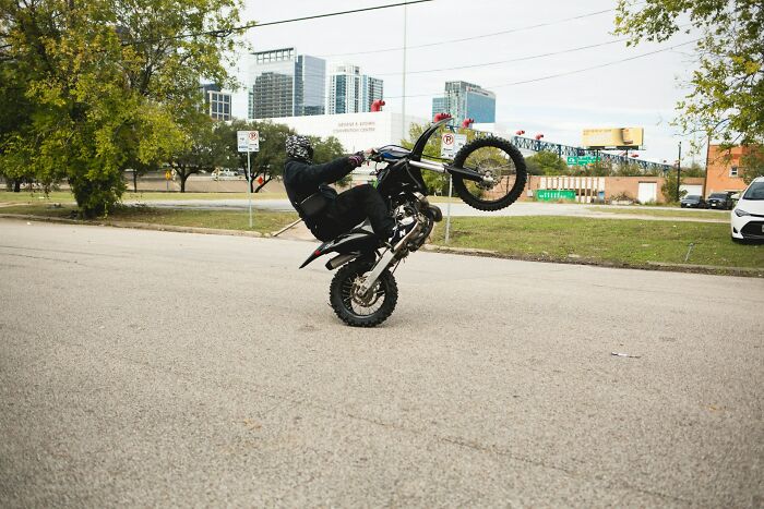Motorcycle rider performing a wheelie on an urban street, illustrating a risky near-death experience moment.