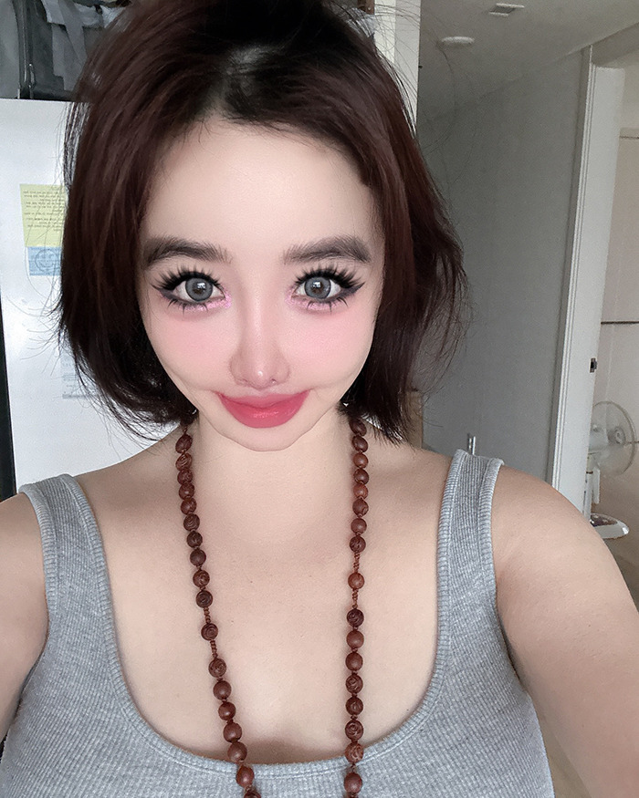 K-Pop icon Park Bom wearing a gray tank top and necklace, showing her drastic plastic surgery transformation.