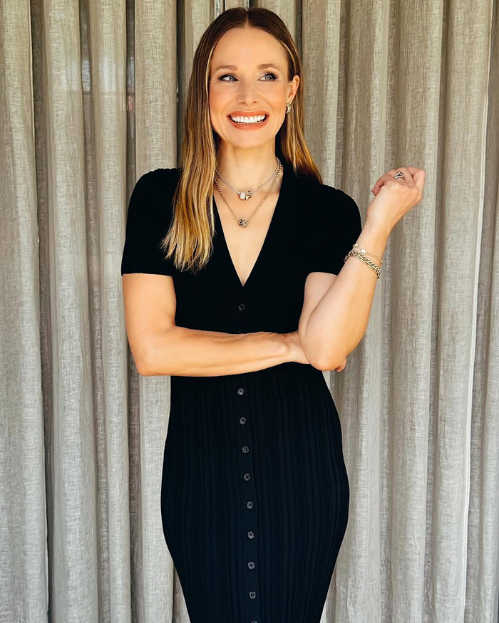 Kristen Bell smiling in a black dress with layered necklaces, representing the discussion around toxic marriage fights.