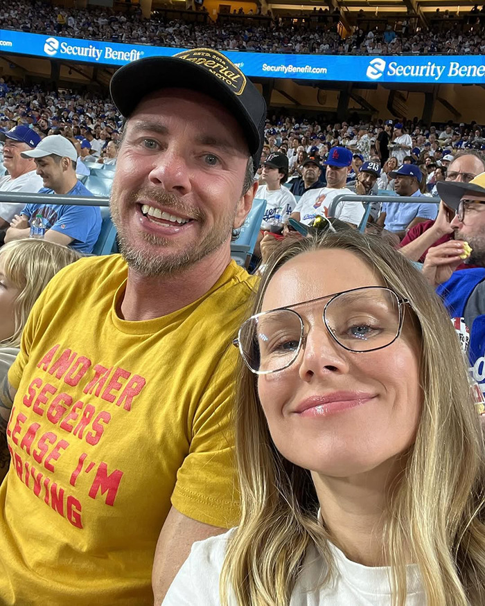 Kristen Bell and Dax Shepard smiling together at a crowded stadium, amid talks of their toxic marriage and blackout fights.