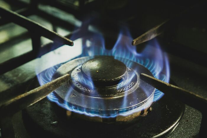 Close-up of a gas stove burner with blue flames, illustrating cooking heat for preparing shrimp jello or similar dishes.
