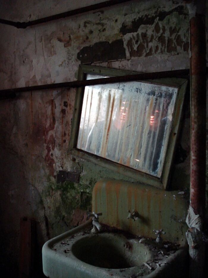 Abandoned bathroom with dirty sink and cracked mirror reflecting a ghostly figure in a creepy photo that makes hearts skip a beat