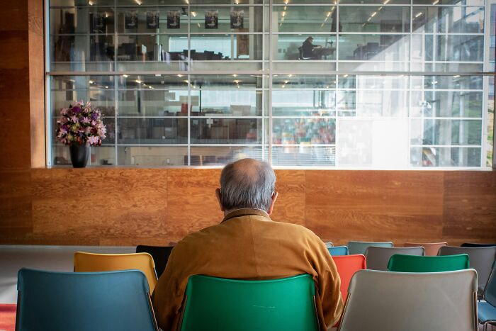 An elderly man sitting alone on colorful chairs in an empty restaurant, representing a painful table for two moment.