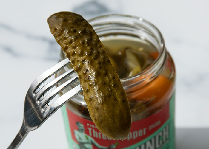 Close-up of a fork holding a pickle above an open jar, unrelated to steak or cows facts.