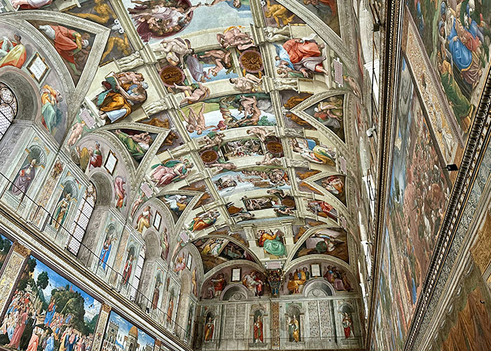 Intricate frescoes cover the ceiling and walls of a historic hall, showcasing detailed scenes and figures.