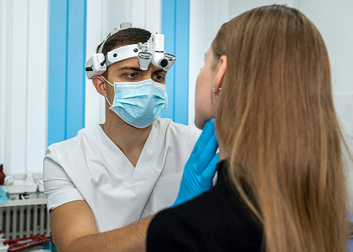 Medical professional wearing magnifying headgear and mask examining a female patient in a clinical setting, related to steak comes from cows.