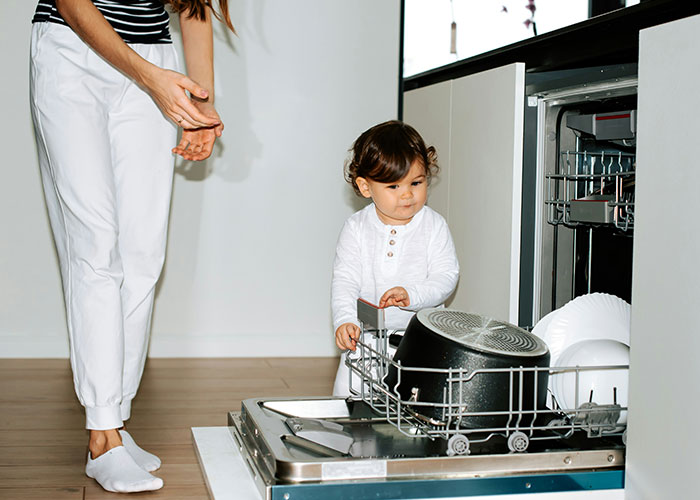 Young child helps load dishwasher with adult nearby, illustrating everyday life and learning moments about steak from cows.
