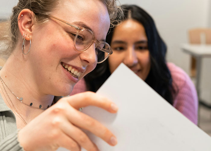 Two women smiling and looking at a paper while discussing steak comes from cows facts together.