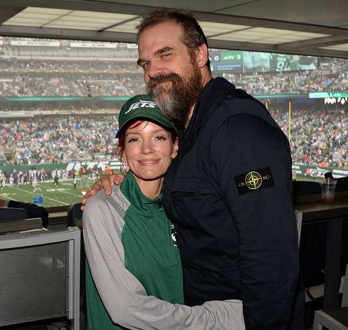 Lily Allen and David Harbour hugging at a stadium during a football game, showing a close moment together.