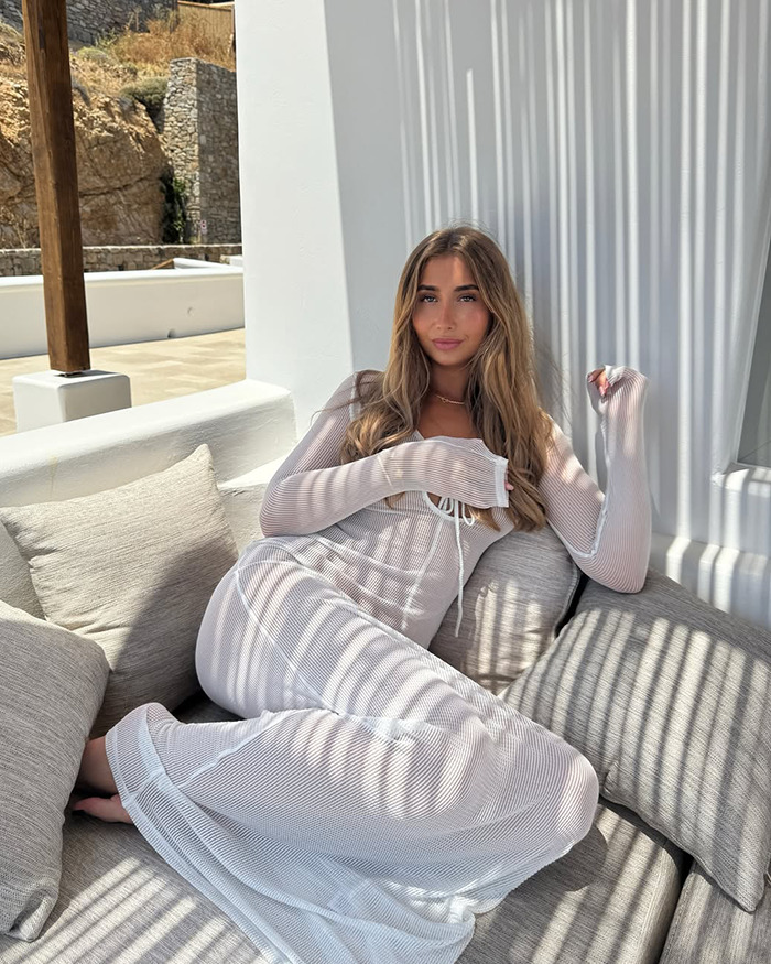 Lily Phillips lounging on a couch indoors wearing a white dress, capturing attention with her relaxed pose and natural look.