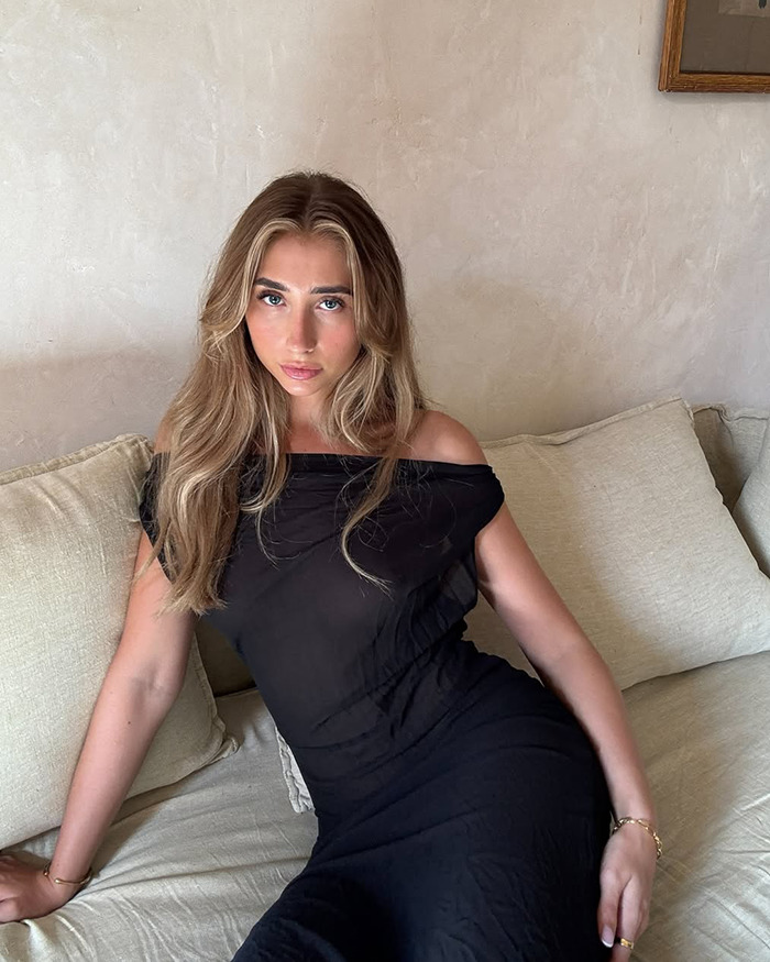 Lily Phillips sitting on a beige couch wearing a black off-shoulder dress, discussing her fame and love of money.