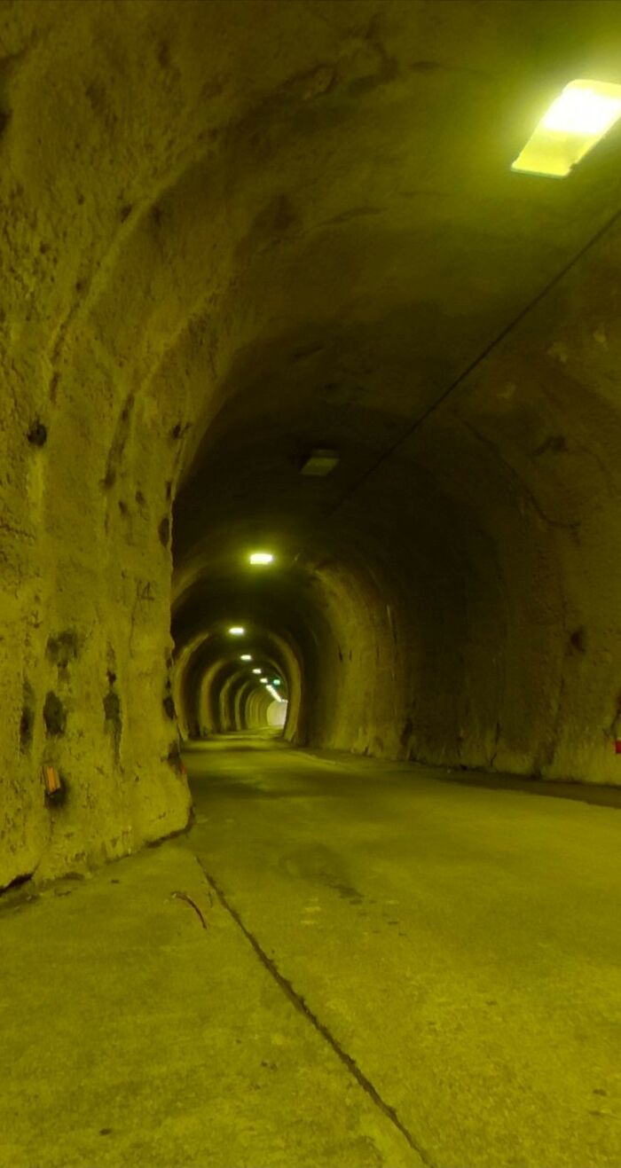 Dimly lit tunnel with rough textured walls, showcasing an unnerving liminal space flooded with yellow light.