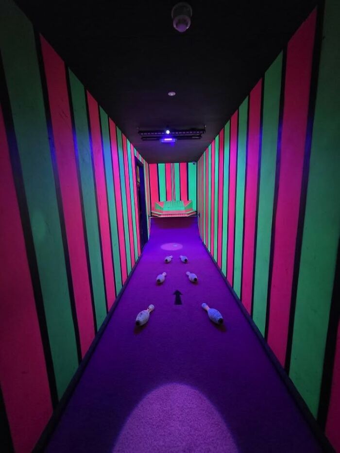 Colorful narrow hallway with bowling pins arranged on the floor, creating a beautiful yet unnerving liminal space.