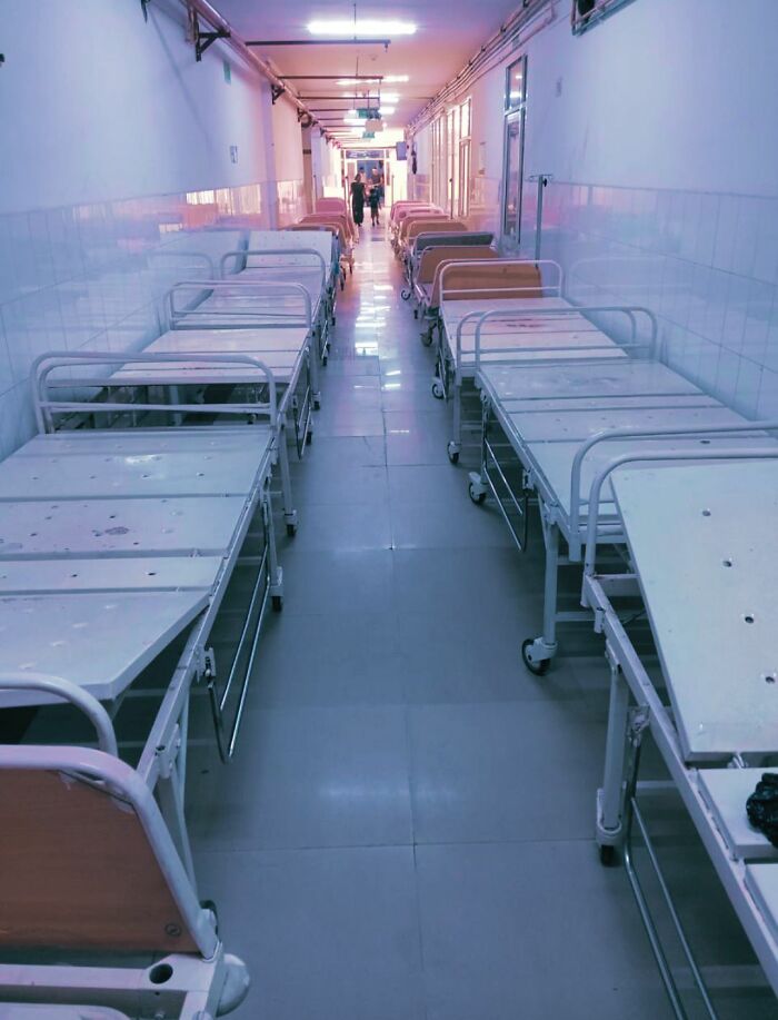 Empty hospital beds lined up in a long, sterile hallway creating a beautiful yet unnerving liminal space atmosphere.