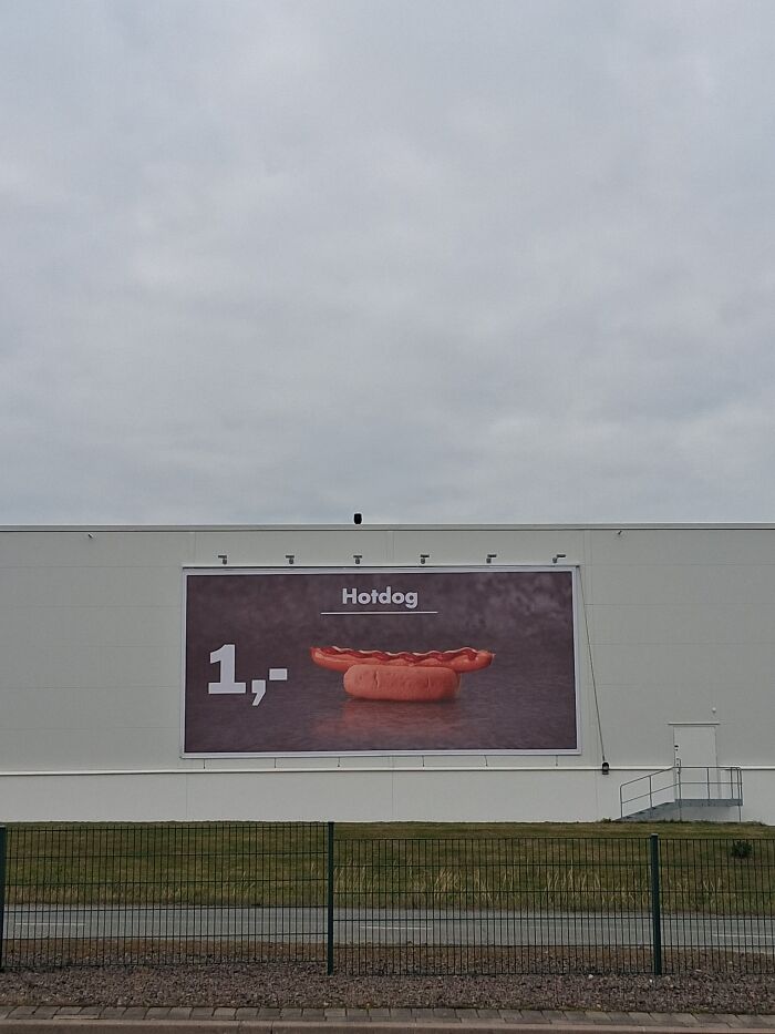 Billboard advertising a hotdog for 1 euro in a stark, empty urban setting reflecting unnerving liminal spaces.