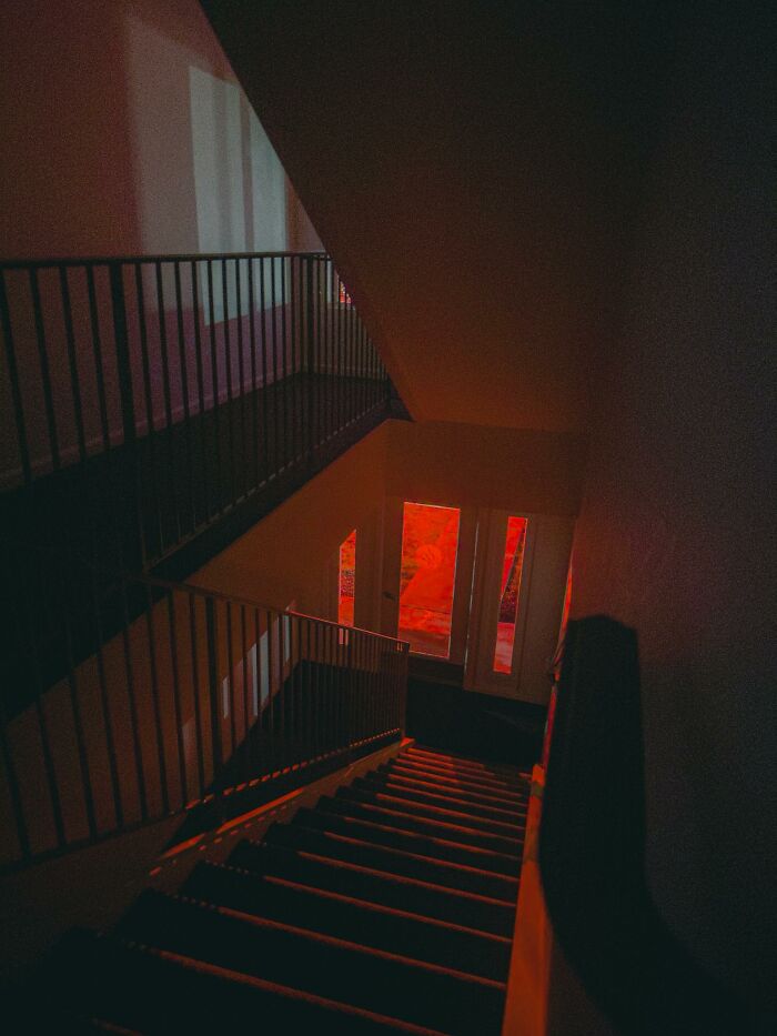 Dimly lit staircase with red-tinted windows creating an eerie and unnerving liminal space atmosphere.