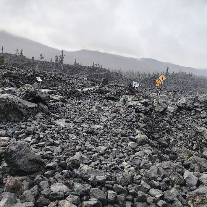 Liminal space of rocky barren terrain with scattered signs and a foggy forested mountain backdrop on a gloomy day