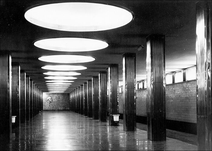 Unnerving liminal space in a long corridor with circular ceiling lights and reflective pillars creating a surreal atmosphere.