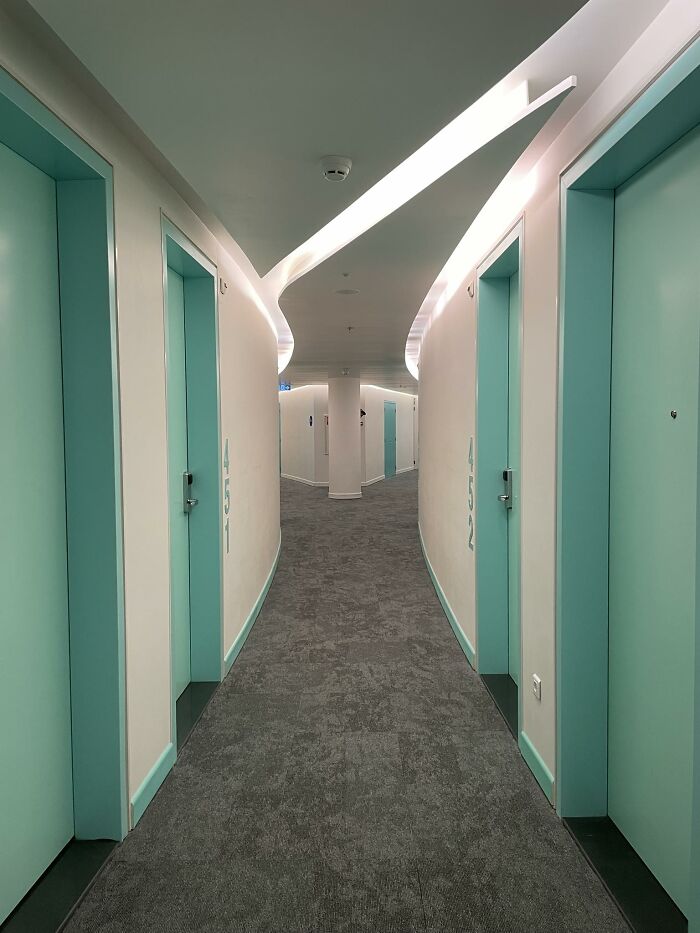 Curved hallway with teal doors and soft lighting creating a beautiful yet unnerving liminal space interior view.