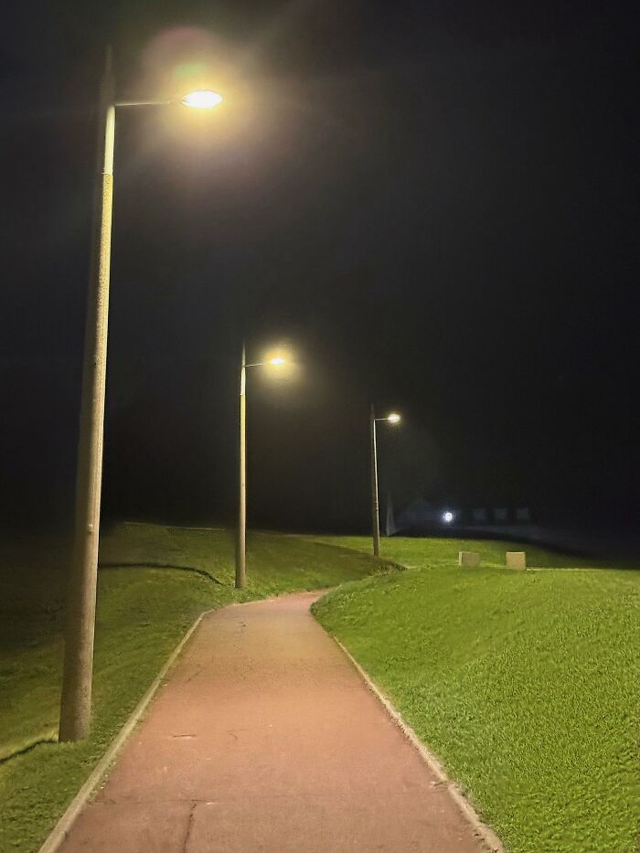 Dimly lit pathway with street lamps casting light over an unsettling liminal space at night.