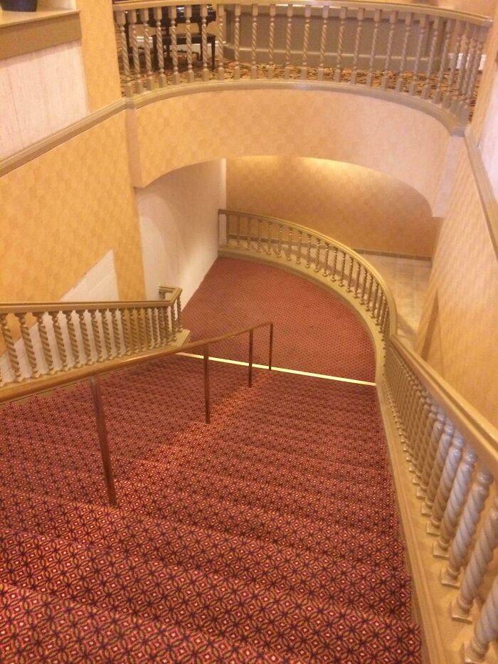 Curved staircase with patterned carpet and wooden railings, showcasing a beautiful yet unnerving liminal space indoors.