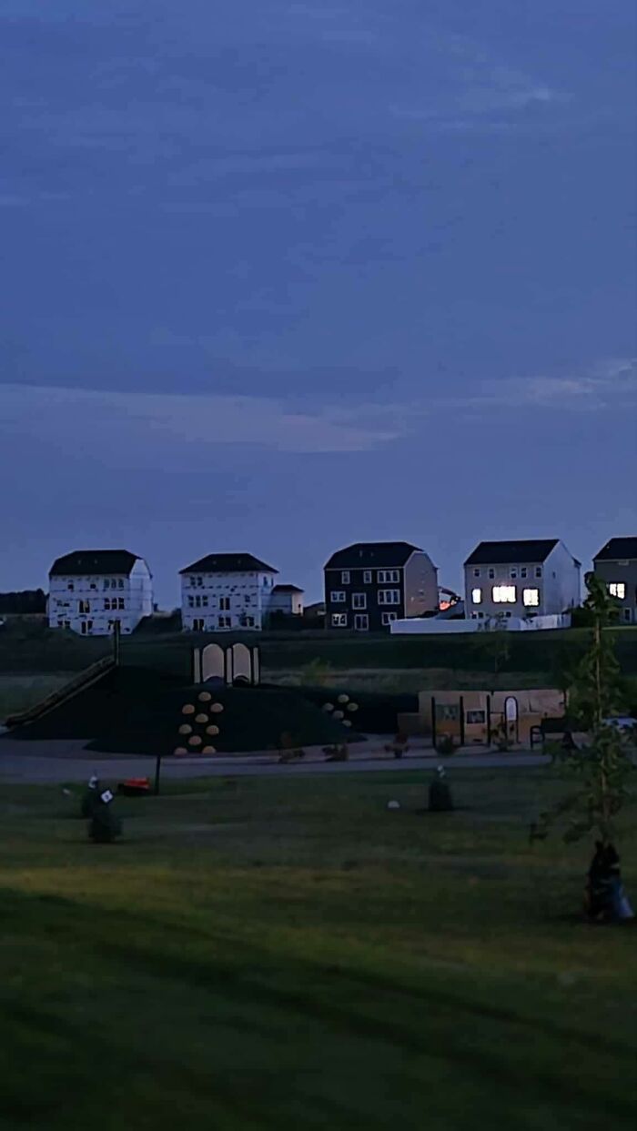 Suburban liminal space at dusk with quiet playground and unnerving rows of houses in the distance.