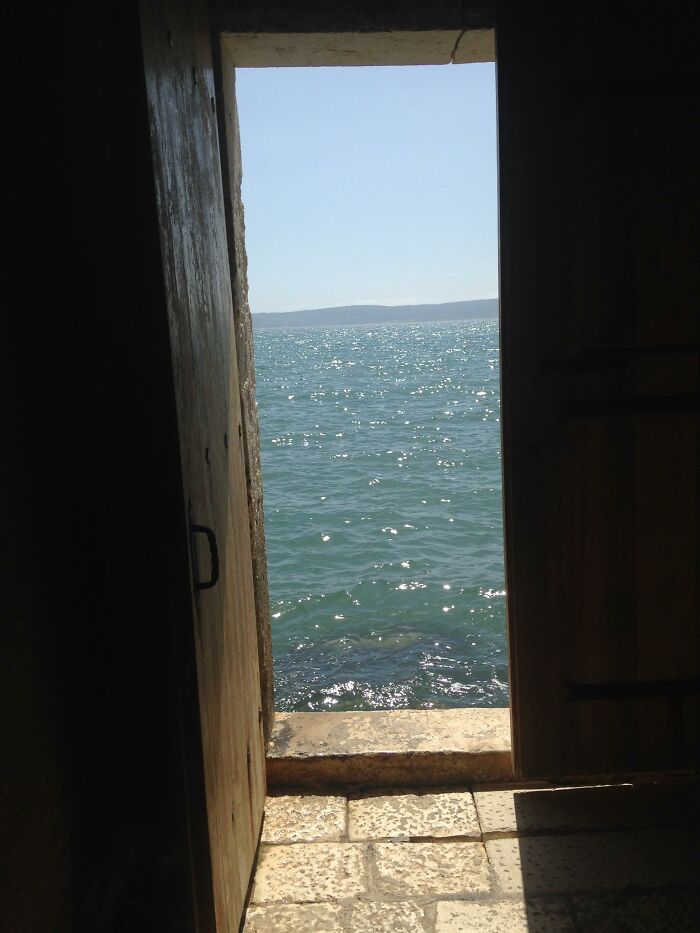 View of sparkling sea through an open doorway creating a beautiful yet unnerving liminal space by the water.