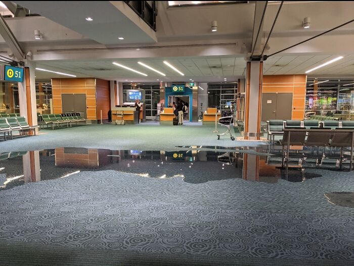 Empty airport terminal with flooded floor creating an unnerving liminal space and reflected ceiling lights