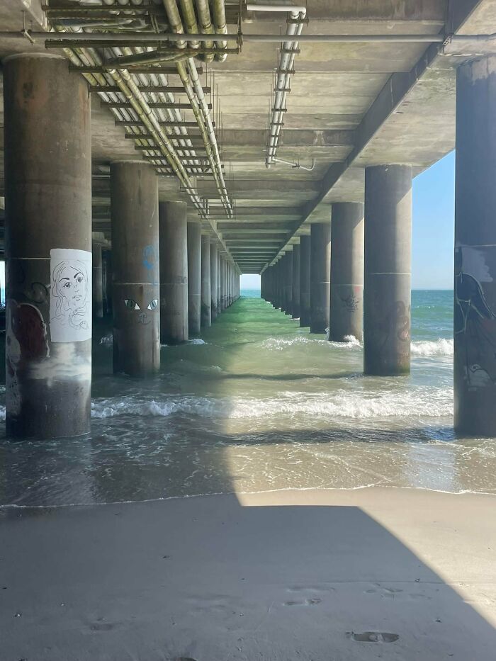 Underneath a pier with concrete pillars, ocean waves create a beautiful yet unnerving liminal space by the shore.