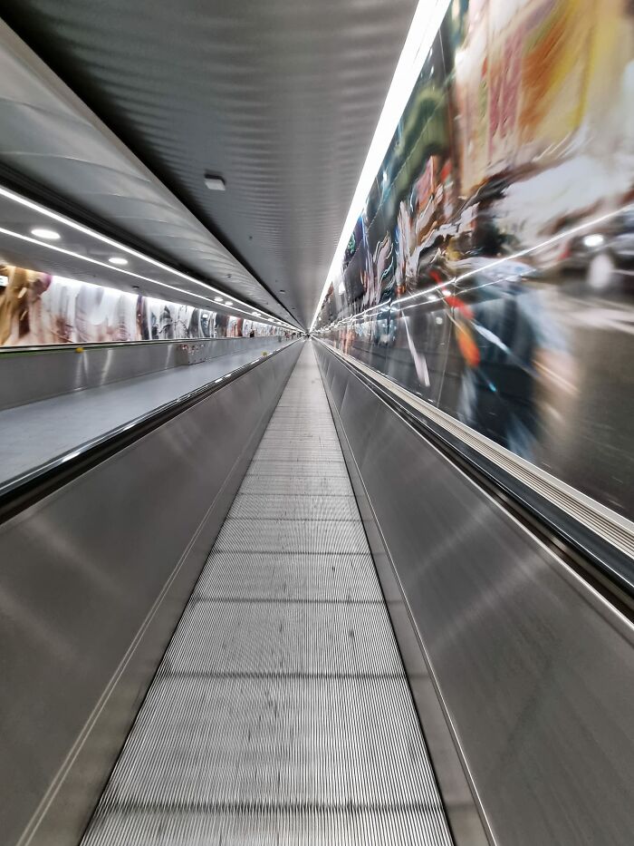 Long, empty liminal space inside a tunnel-like corridor with reflective walls creating a beautiful yet unnerving effect.