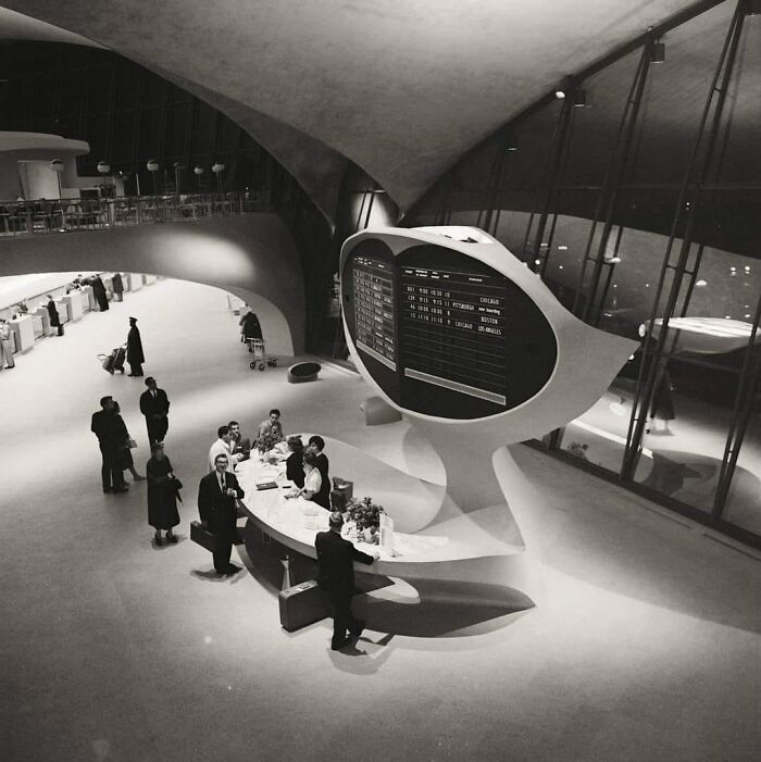 Vintage airport terminal with futuristic design, featuring a flight information display and travelers in a liminal space.