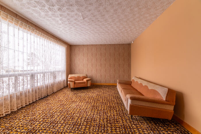 Empty vintage living room with patterned carpet and beige furniture, creating a beautiful yet unnerving liminal space.