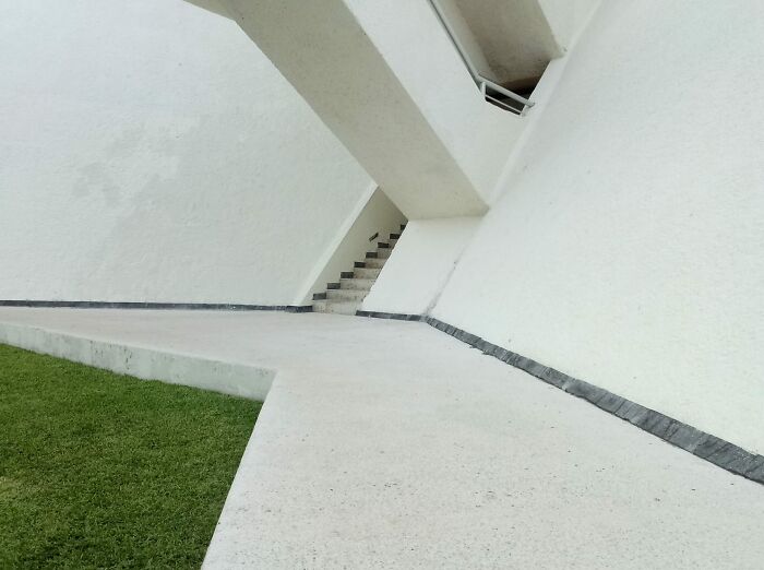 Minimalist white architectural space with sharp angles and stairs, creating a beautiful yet unnerving liminal space.