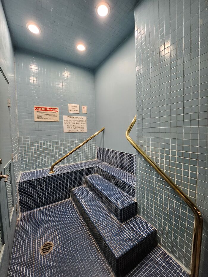Blue tiled spa area with stairs and brass handrails, showcasing a beautiful yet unnerving liminal space.