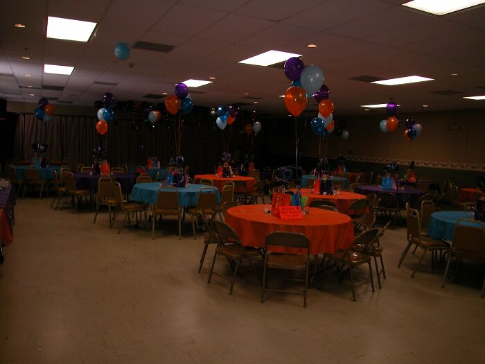 A dimly lit event room with colorful balloons and round tables, evoking beautiful yet unnerving liminal spaces.