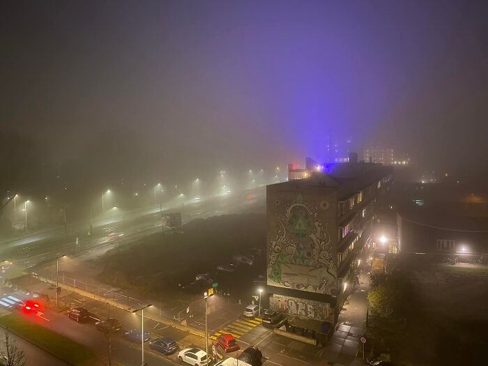 Foggy urban scene at night showing liminal spaces with streetlights, a graffiti-covered building, and a quiet city road.