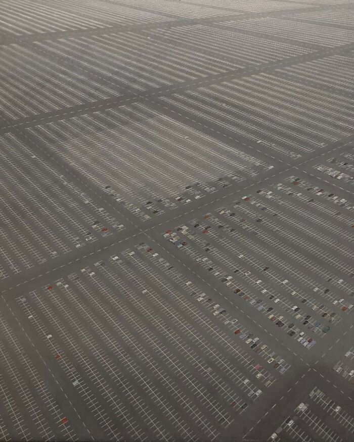 Aerial view of an expansive and unnerving liminal parking lot space with sparse cars creating a surreal pattern