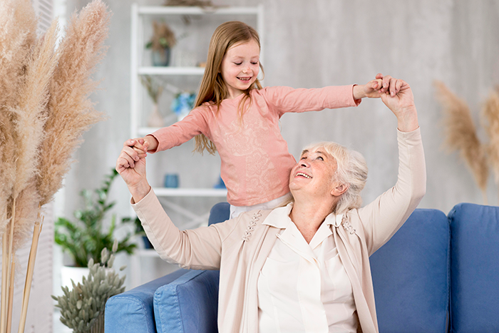 Elderly woman and young girl smiling and holding hands in a bright room, contrasting stepdaughters disown stepmother drama.