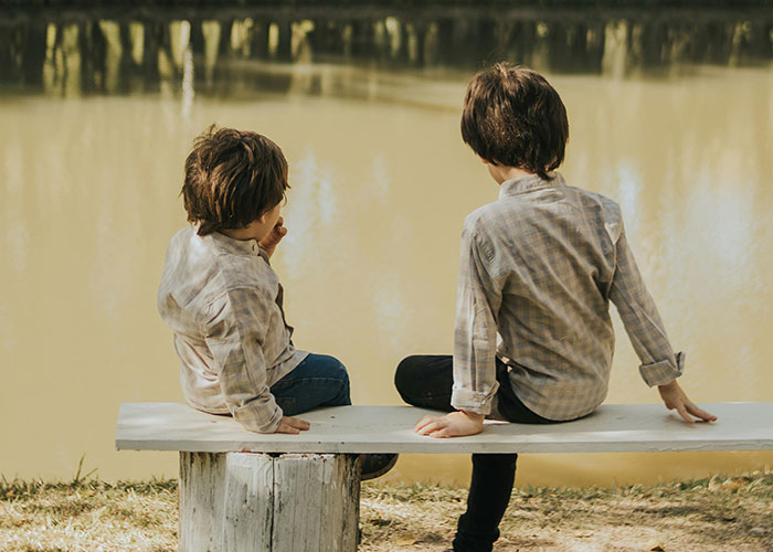 Two young boys sitting on a bench by a pond, representing children affected by foster care and family changes.