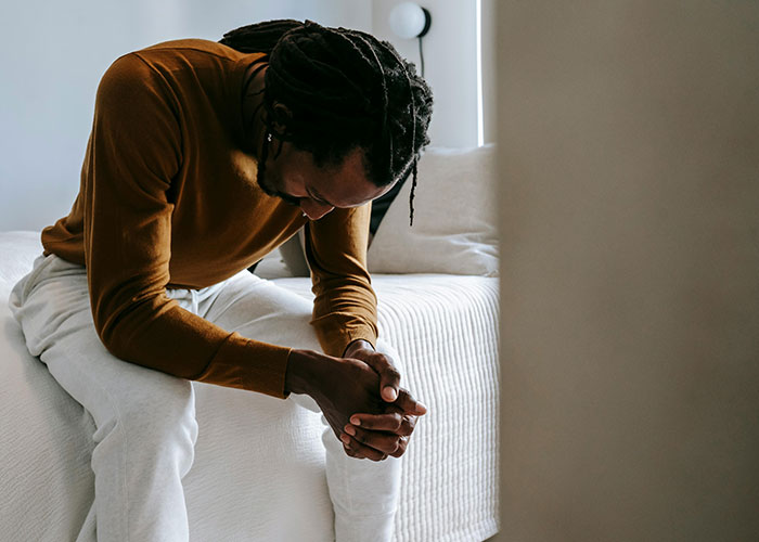 Man sitting on bed, deep in thought, reflecting on a situation involving saving niblings from foster care.