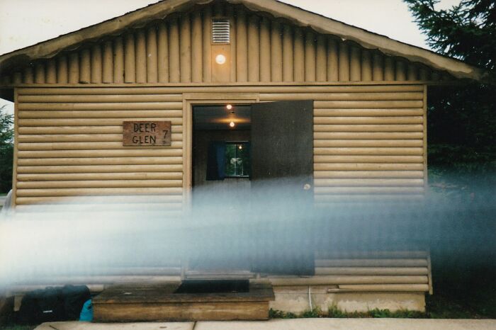 Creepy photo of a cabin with a mysterious mist or fog passing in front, creating an eerie atmosphere.