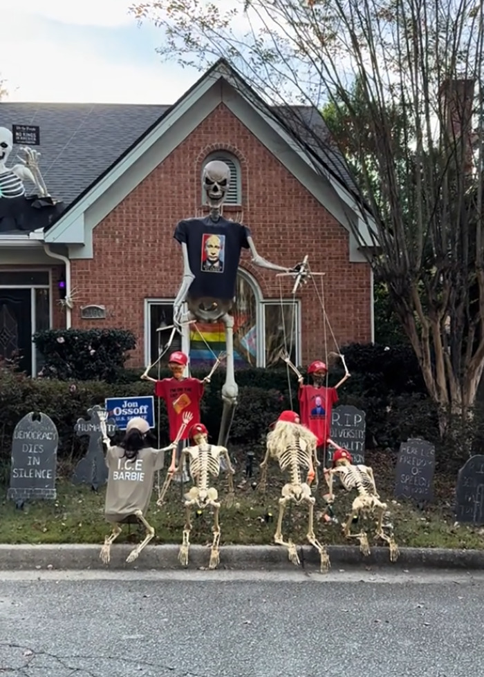 Elaborate anti-MAGA Halloween display with skeleton puppets wearing political shirts and red hats in a front yard.