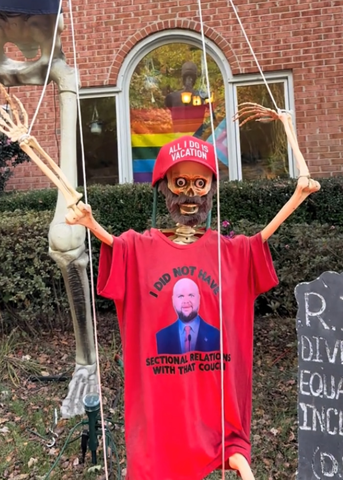 Skeleton figure in an anti-MAGA Halloween display wearing a red hat and shirt with a humorous political message.